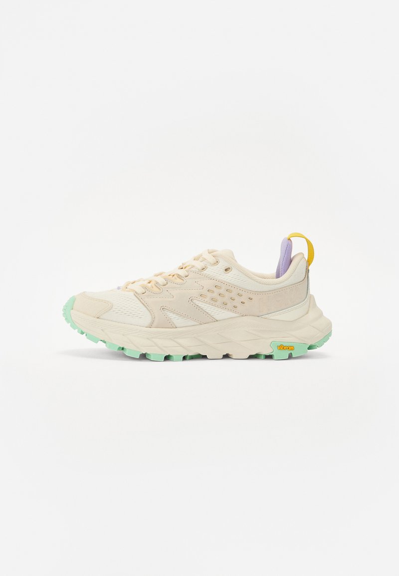Beige Sport Schuh mit strukturiertem Mesh und Wildlederüberzügen, grünem Gummiaußensohle, lilafarbenem Akzent an der Ferse und gelbem Zugband. Mit Vibram-Branding.
