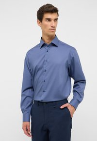 Camicia button-up azzurro chiaro con colletto aperto, maniche lunghe e tessuto liscio; presenta cinque bottoni scuri lungo la parte anteriore.