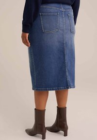 Gonna in denim di blu medio con taglio dritto, di lunghezza media, dotata di due tasche posteriori e orlo pulito, abbinata a stivaletti alla caviglia marroni.