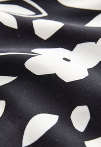 Zwarte stof met een gladde textuur, voorzien van grote witte bloemenpatronen. Het ontwerp bevat verschillende vormen en effen kleuraccenten.