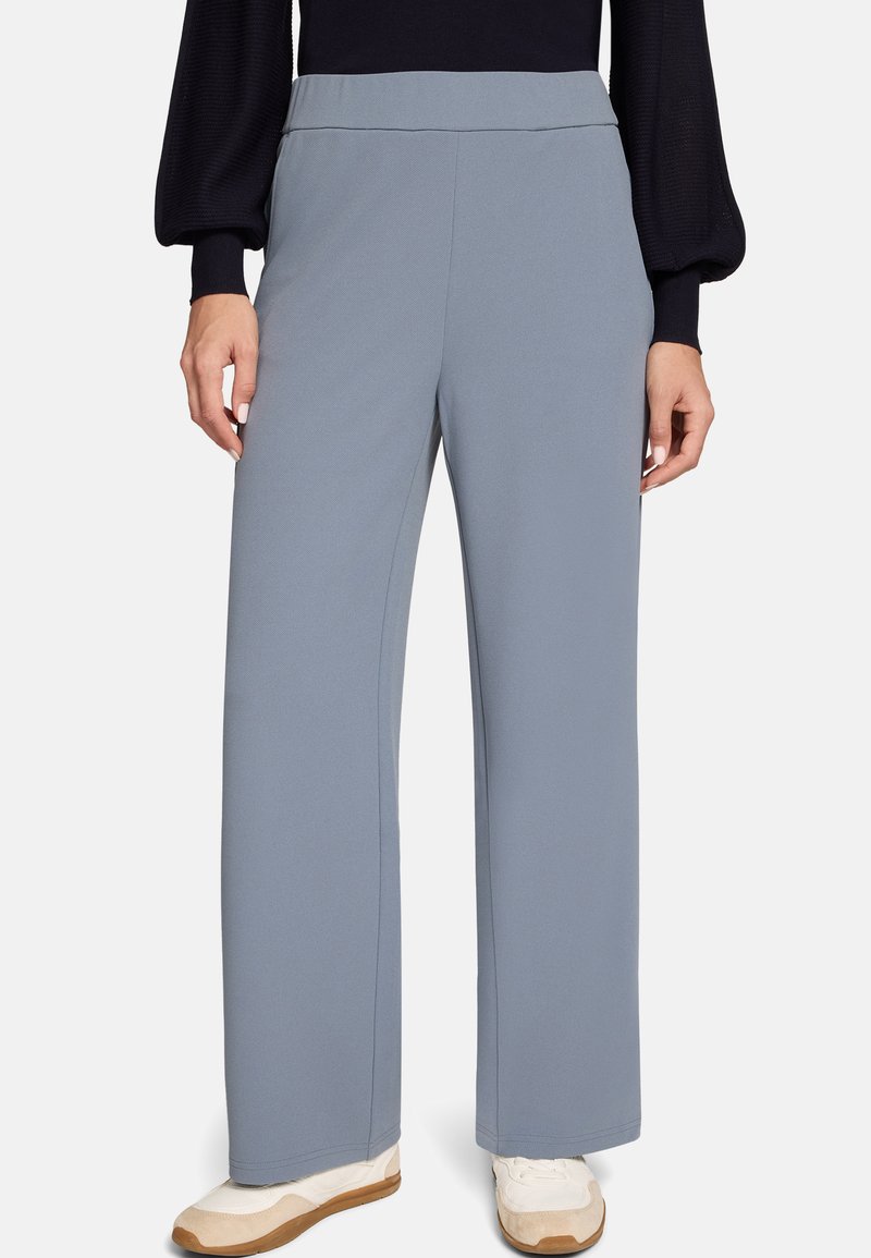 Pantalon gris clair à jambes larges réalisé en tissu lisse. Il présente une taille haute et une silhouette nette et ajustée, porté avec des baskets blanches.
