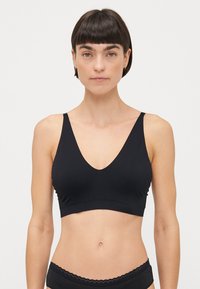 Zwarte bralette met een diepe V-hals, gemaakt van gladde stof. Beschikt over brede bandjes en een naadloos ontwerp zonder zichtbare hardware.