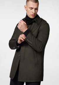 Beżowy płaszcz trench z pagonami na ramionach, długimi rękawami i brązowymi guzikami. Miękka tkanina, dopasowany krój i kieszenie boczne.