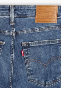 Vaqueros de denim con un color azul desvaído, que presentan una parche de cuero en la parte trasera de la cintura y una etiqueta roja de Levi's en el bolsillo trasero.