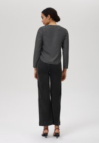 Svart-og-hvitt stripete langermet topp, kombinert med høyt liv og vide sorte jeans. Har en rett nederkant og en avslappet passform.