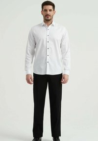 Chemise blanche à manches longues avec des boutons foncés, associée à un pantalon noir. Tissu lisse, coupe structurée, design classique.