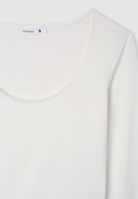 Biała bluzka z długim rękawem i okrągłym dekoltem, wykonana z gładkiego materiału. Posiada małą metkę marki przy dekolcie. Prosty i minimalistyczny design.