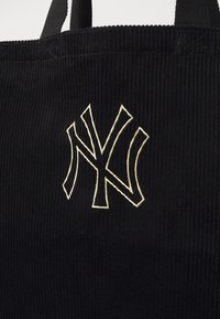 Μαύρη τσάντα tote από κοτλέ με διπλές λαβές, διακοσμημένη με κεντημένο λευκό λογότυπο της Νέας Υόρκης. Υφή με κάθετες ραβδώσεις.