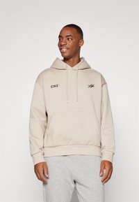 Felpa beige con tasca frontale, cappuccio con stringa e loghi neri "CNZ" e una grafica. Pantaloni della tuta grigi, in tessuto morbido e vestibilità comoda.