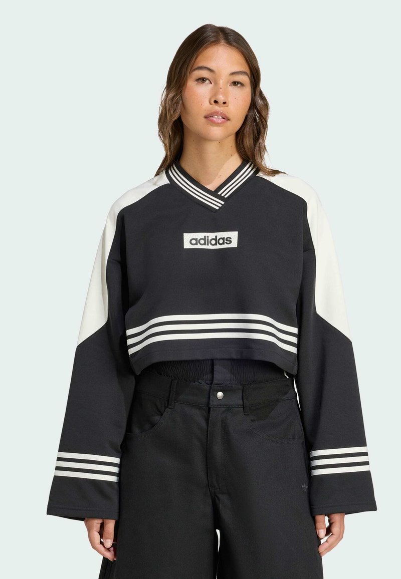 Sweatshirt noir coupé avec des manches blanches et trois bandes blanches à l'ourlet. Il présente un col en V et un logo adidas brodé sur le devant.
