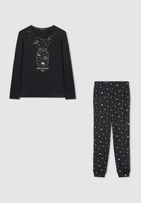 Maglietta nera a maniche lunghe con illustrazione di barattolo e spazio, testo "Guarda la tua magia crescere", abbinata a pantaloni neri coperti da motivi a tema spaziale bianchi.