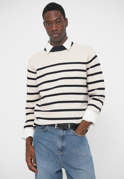 Prugasta puloverica u bež i mornarsko plavoj boji, rebraste teksture, s ovratnikom i bijelim manžetama. Nosila se s svijetloplavim trapericama i crnim remenom.