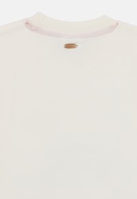 Cremefarbener Baumwoll-T-Shirt mit einem gerippten Rundhalsausschnitt. Bemerkenswerte Details sind ein kleines Markenetikett, das am Rücken des Halsausschnitts angenäht ist.