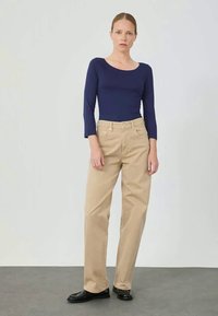 Marineblauw langarmshirt, lichtbeige rechte broek en zwarte schoenen, tegen een neutrale achtergrond. Eenvoudig en minimalistisch ontwerp.