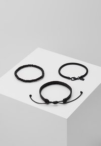 Tre svarte armbånd: ett perlearmbånd, ett flettet med lås og ett justerbart snorarmbånd med knute. Alle har forskjellige teksturer.