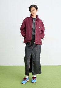 Bordeaux ritsjack, gestreept zwart-wit shirt eronder, zwarte leren rok met een voorknip, blauwe sneakers met rode accenten.