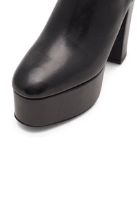 Čierna kožená topánka na vysokom opätku s guľatou špičkou a hrubou platformou. Hladký povrch s lesklým finišom a jasne definovanými okrajmi.