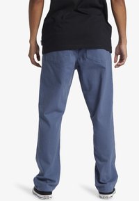 Blue cotton pants with a relaxed fit, featuring back pockets and visible stitching, paired with black sneakers.