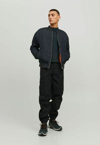 Giacca bomber della marina con interno arancione, pantaloni cargo neri e sneakers multicolori con accenti grigi. Texture liscia, chiusura a zip.