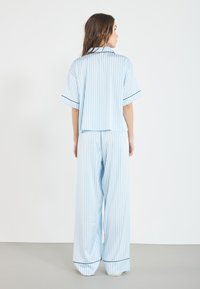 Blue and white striped pajama set with a short-sleeve shirt and wide-leg pants, featuring contrasting black trim along the edges.