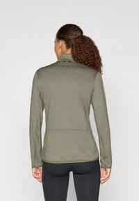 Olivenfarbener, langärmliger Sportoberteil aus strukturiertem Stoff mit hohem Kragen und Taschendetail auf der Rückseite. Verfügt über eine figurbetonte Passform und elastischen Stoff.