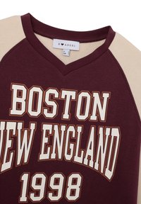 Bordeaux en crèmekleurige sweatshirt met "BOSTON NEW ENGLAND 1998" in wit en bruin erop gedrukt. Heeft een v-hals en raglan mouwen.