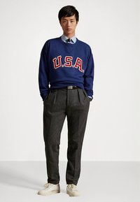 Μπλε φούτερ με γράμματα «U.S.A.», γκρι παντελόνι με πτυχώσεις και μπεζ αθλητικά παπούτσια. Η εμφάνιση περιλαμβάνει πουκάμισο με γιακά κάτω από το φούτερ.