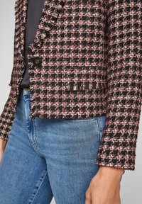 Svart och rosa tweedjacka med fransade kanter, med enknappsslutning och framficka, i kombination med blå denimjeans.