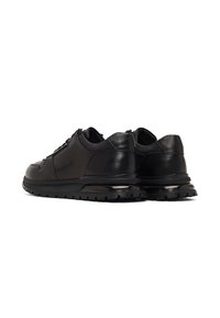 Par de zapatillas de cuero negro con suelas texturizadas y amortiguación de aire visible sobre fondo blanco, vistas desde la parte trasera.