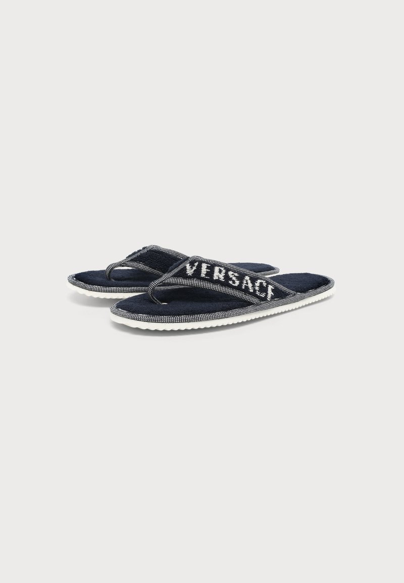 Infradito Versace blu navy con suola bianca e logo sulle fasce, esposte su uno sfondo grigio chiaro.