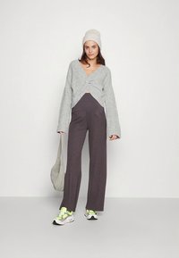 Pull enveloppant en maille grise, pantalon côtelé marron foncé taille haute, bonnet gris clair, et baskets multicolores, avec un sac à bandoulière gris doux.