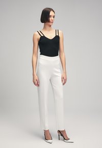 Zwarte geribbelde top met dubbele bandjes, gecombineerd met strakke witte broek en zwart-witte puntige hakken. Eenvoudige, strakke lijnen overal.