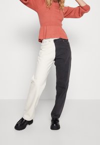 Jean bicolore avec une jambe en crème et l'autre en gris foncé, avec une coupe décontractée et des coutures bien visibles. Associé avec un top peplum corail.