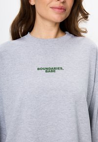 Grijze sweatshirt gemaakt van zachte stof, met een ronde hals en een losse fit, met "BOUNDARIES, BABE" geborduurd in donkergroen.