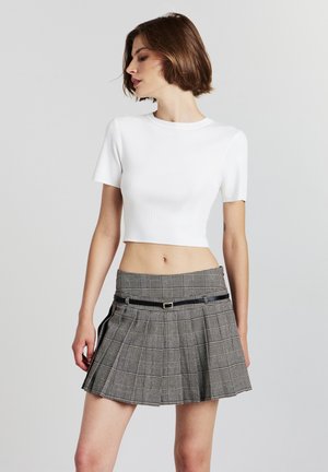 T-shirt cropped blanc à côtes associé à une mini-jupe plissée à carreaux noirs et gris, avec une ceinture noire en accent et un tissu structuré.