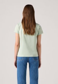 Lys grøn kortermet t-skjorte laget av bomull, med rund halslinning og en avslappet passform, sammen med høytlivede blå denimjeans.
