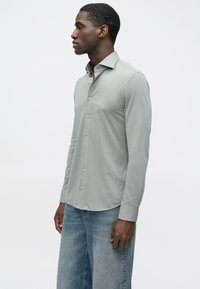 Világosszürke hosszú ujjú ing klasszikus gallérral, gombos előlappal és puha textúrával. Kék, bőszárú farmernadrággal párosítva.