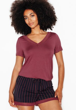 Donna con i capelli ricci che indossa una maglietta bordeaux a maniche corte con scollo a V e pantaloncini blu navy con strisce bordeaux e rifinitura in pizzo.