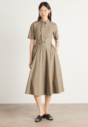 Beige knappoppkjørt kjole med korte ermer, belte i midjen og A-line skjørt. Har jevn tekstur og minimalistisk design. Sorte sklisko.
