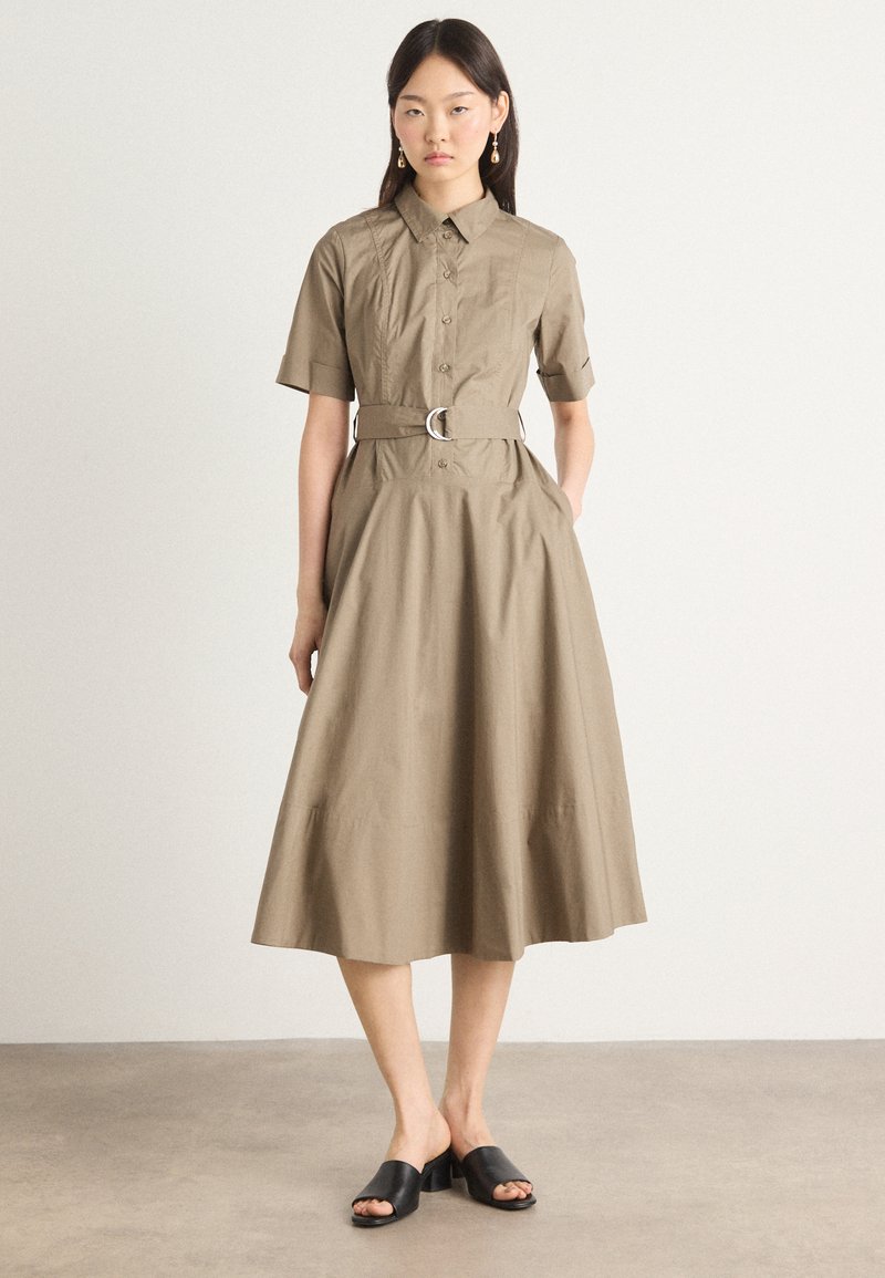Tan button-up dress with short sleeves, a belted waist, and A-line skirt. Features smooth texture and minimalistic design. Black slide-on shoes.