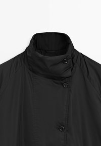 Black high-neck jacket with three visible buttons and a smooth, slightly shiny fabric.