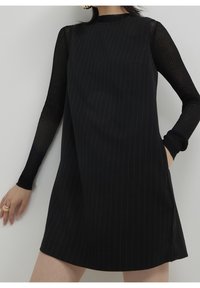 Svart klänning med vertikala ränder. Har långa genomskinliga ärmar och en enkel rund halsringning. Materialet framstår som slätten, med en lätt lyster.