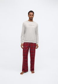 Hanorac gri cu logo și pantaloni de pijama în carouri roșii. Hanoracul are mâneci lungi, manșete ribbate și decolteu rotund. Pantalonii au o croială lejeră.