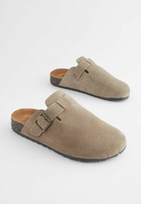 Sabots en suède à enfiler de couleur marron clair avec une sangle et une boucle. Surface texturée, semelle en liège et conception à talon ouvert.