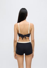 Σετ μπικίνι σκούρου ναυτικού μπλε με υφή. Το τοπ έχει ρυθμιζόμενους κρεμ ιμάντες και λεπτομέρεια φιόγκου στο πίσω μέρος· το κάτω μέρος διαθέτει κρεμ ζώνη στη μέση.