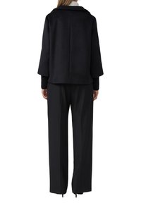 Schwarze Wolle-Mischung cropped Jacke mit einem umgeschlagenen Kragen und weiten Ärmeln, kombiniert mit maßgeschneiderten schwarzen Hosen im geraden Schnitt.