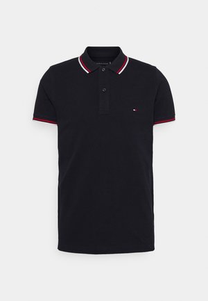 Schwarzes Polohemd mit kurzen Ärmeln, rot-weiß gestreiftem Kragen und Ärmelsäumen, Zwei-Knopf-Leiste und kleinem Logo auf der linken Brust.