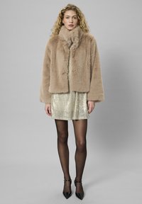 Bežna umetna krzna jakna z visokim ovratnikom, v kombinaciji s kratko obleko z zlatimi bleščicami in črnimi nogavicami. Črne stiletto pete dopolnjujejo videz.