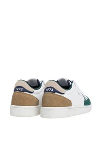 Baskets blanches avec des détails en daim vert, contrefort beige et une étiquette navy avec "1973". Présente un dessus en cuir lisse et une semelle texturée.