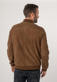 Giacca in suede marrone con colletto strutturato, polsini e orlo a coste. Presenta un design pulito e minimalista con dettagli di cuciture verticali.